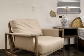 A beige chair with a wooden frame, a small table with a vase, and a bed with a woven headboard. - Signy House City Center (Ho Chi Minh City)