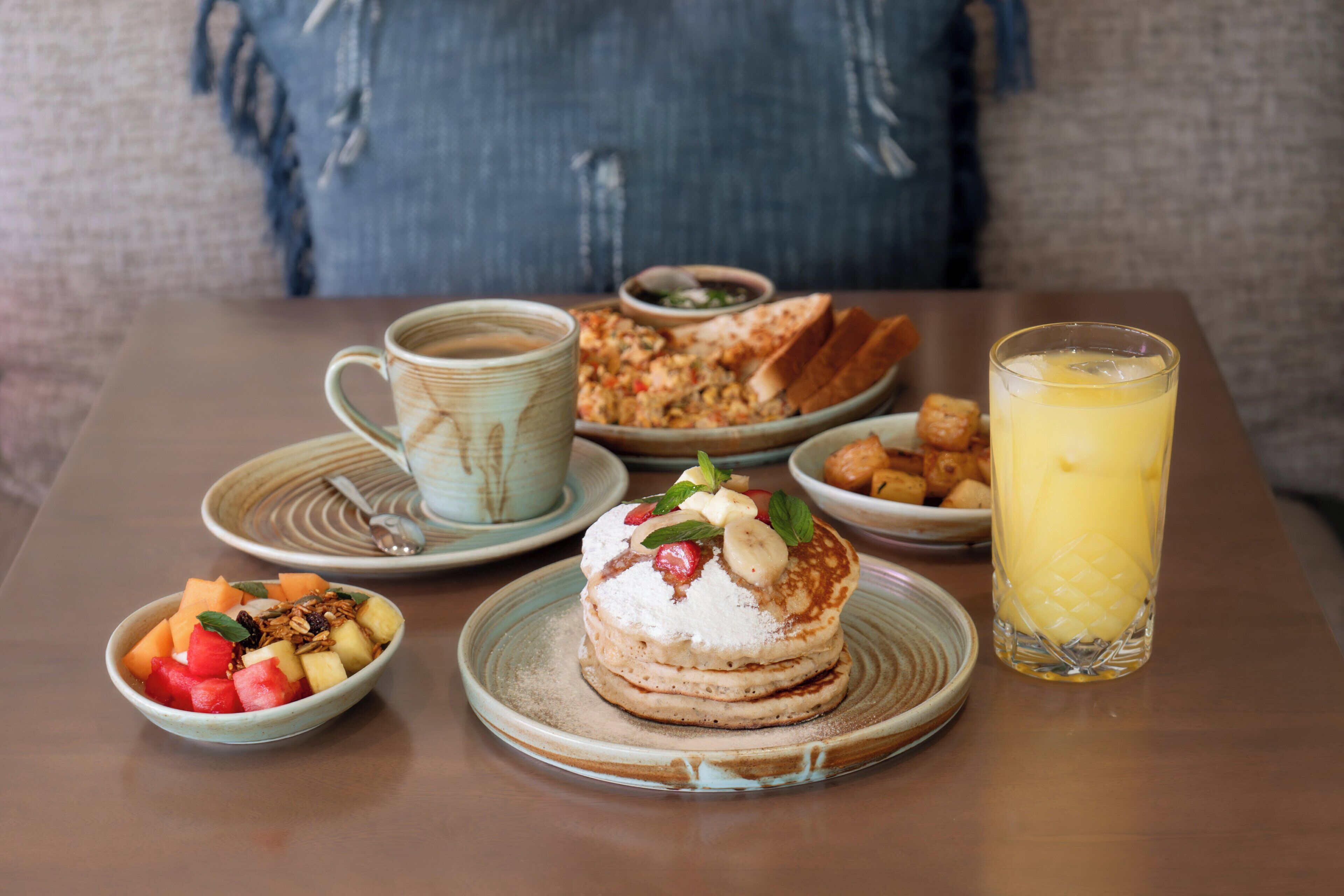 A breakfast setting with pancakes, fruit, a cup, and a glass of juice on a table.