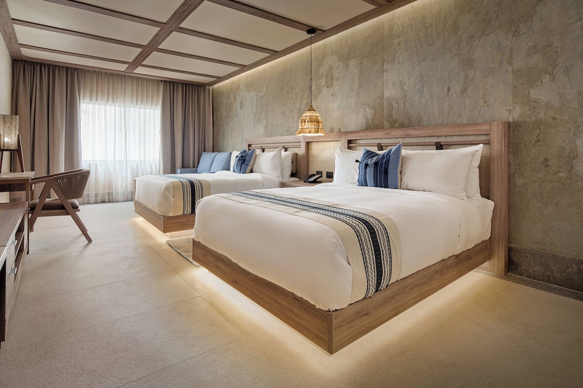 A hotel room with two beds, a desk, and a chair.