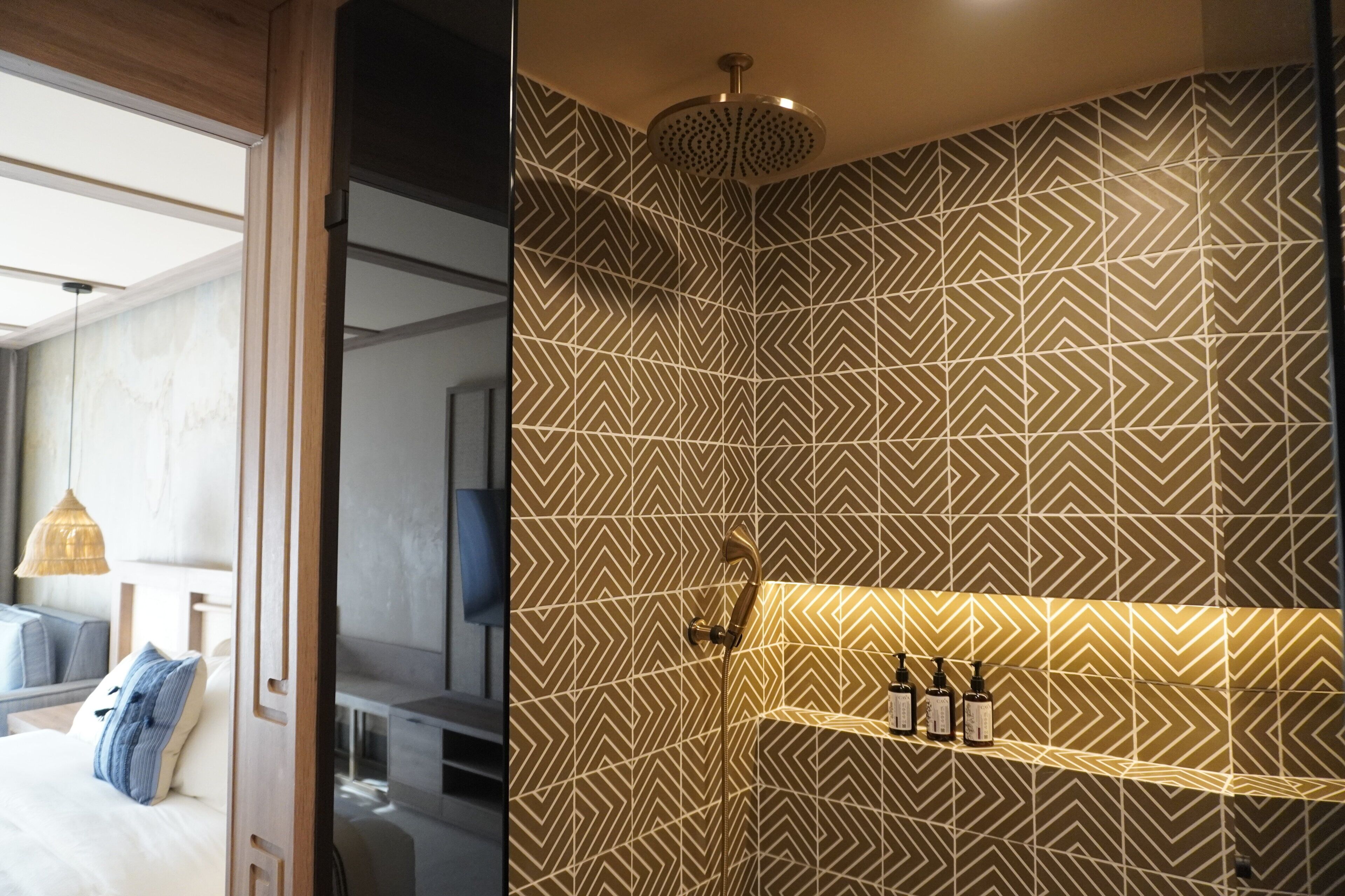 Una habitación de hotel moderna con cama, mesita de noche y baño con azulejos estampados y ducha.