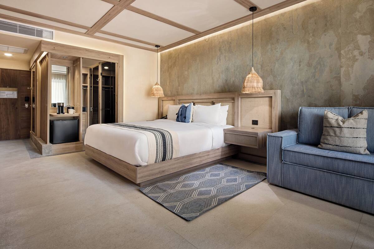 A modern hotel room with a large bed, bedside tables, a sofa, and a patterned rug.