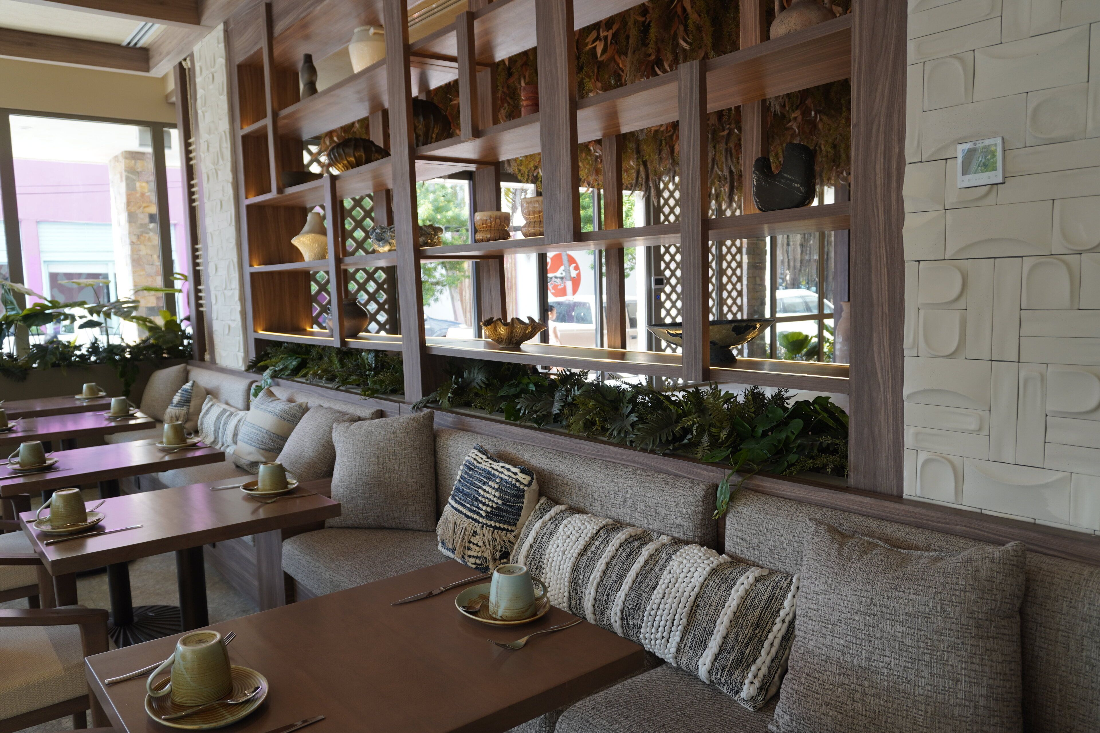 A restaurant with a long bench seating area, wooden tables, and shelves with decorative items.