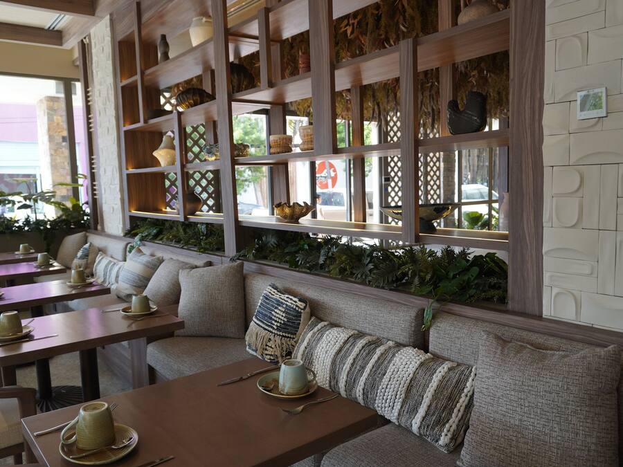 A restaurant with a long bench seating area, wooden tables, and shelves with decorative items.
