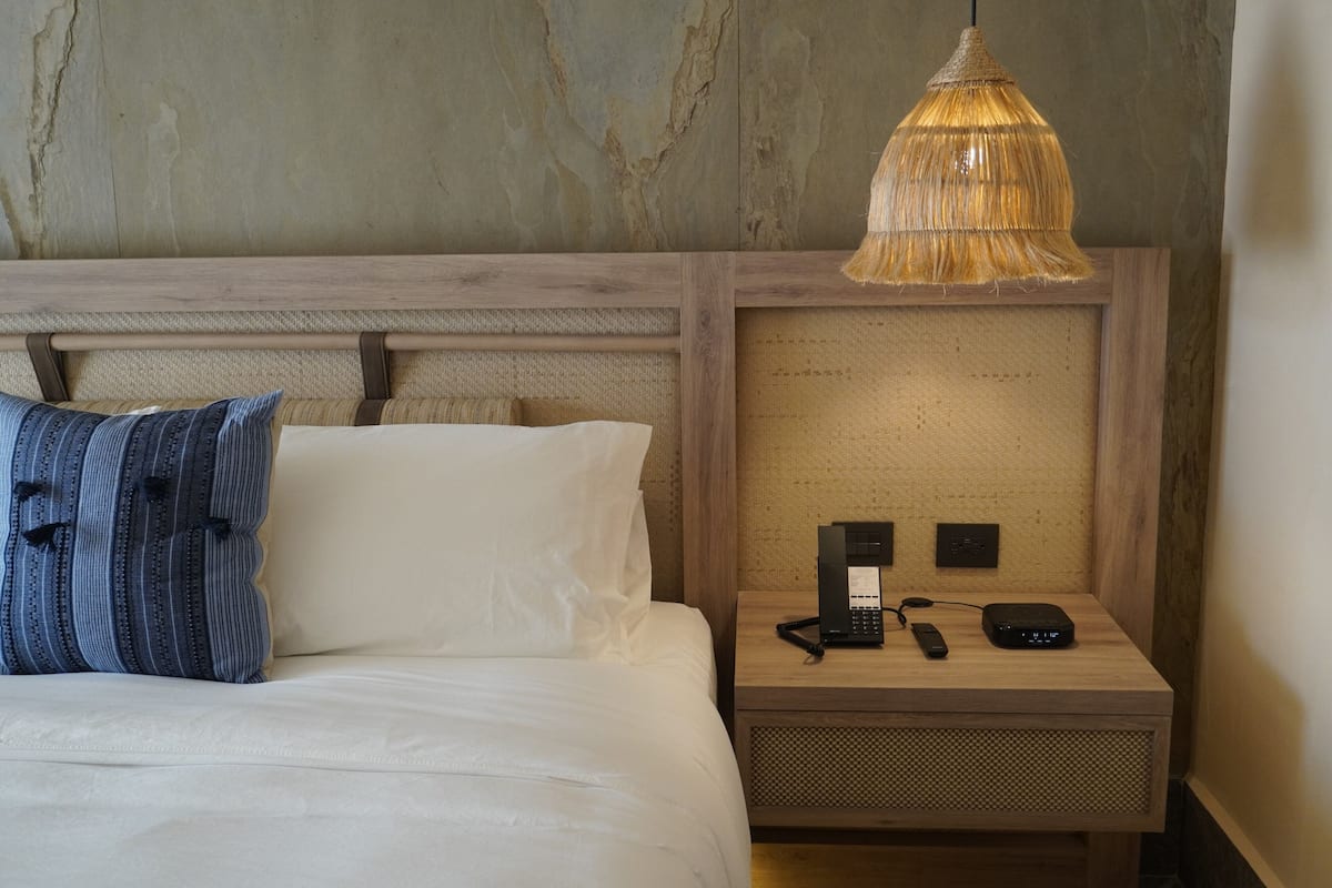 A hotel room with a bed, a nightstand with a telephone and a power strip, and a textured wall.