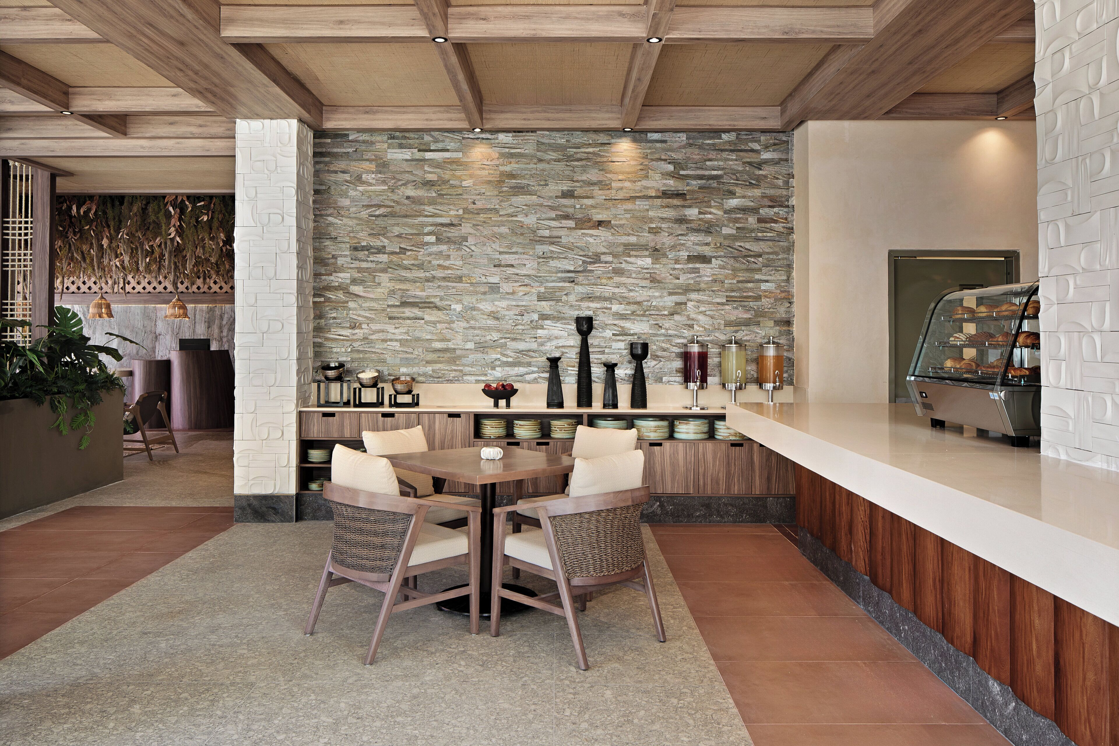 A modern kitchen with a stone backsplash, wooden ceiling beams, and a long counter with a glass display case.