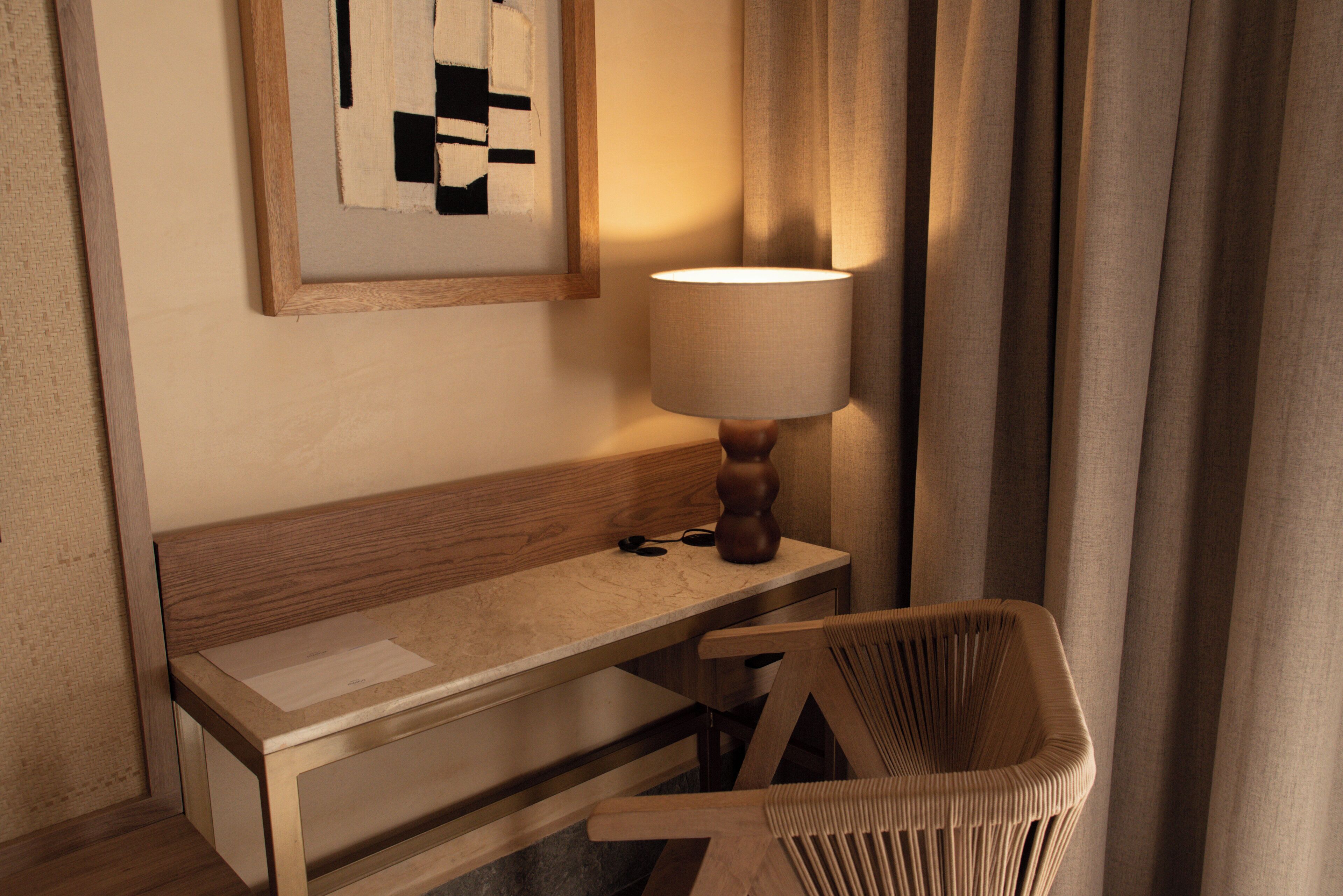 Una camera d'albergo con una panca di legno, un tavolo, una lampada e un quadro astratto appeso alla parete.