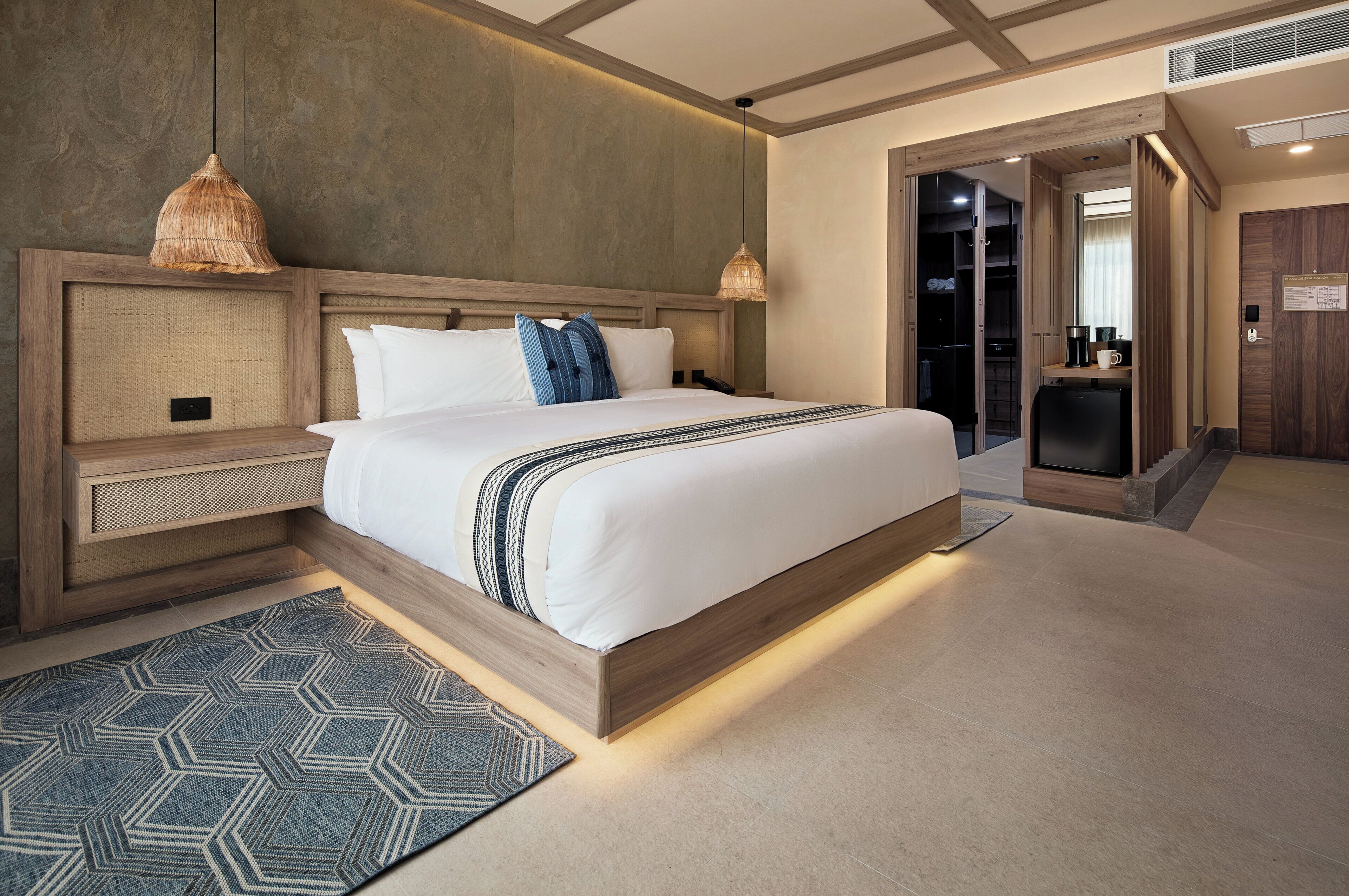 Ein modernes Hotelzimmer mit einem großen Bett, einem Holz-Kopfteil, einem integrierten Schreibtisch und einem begehbaren Kleiderschrank.