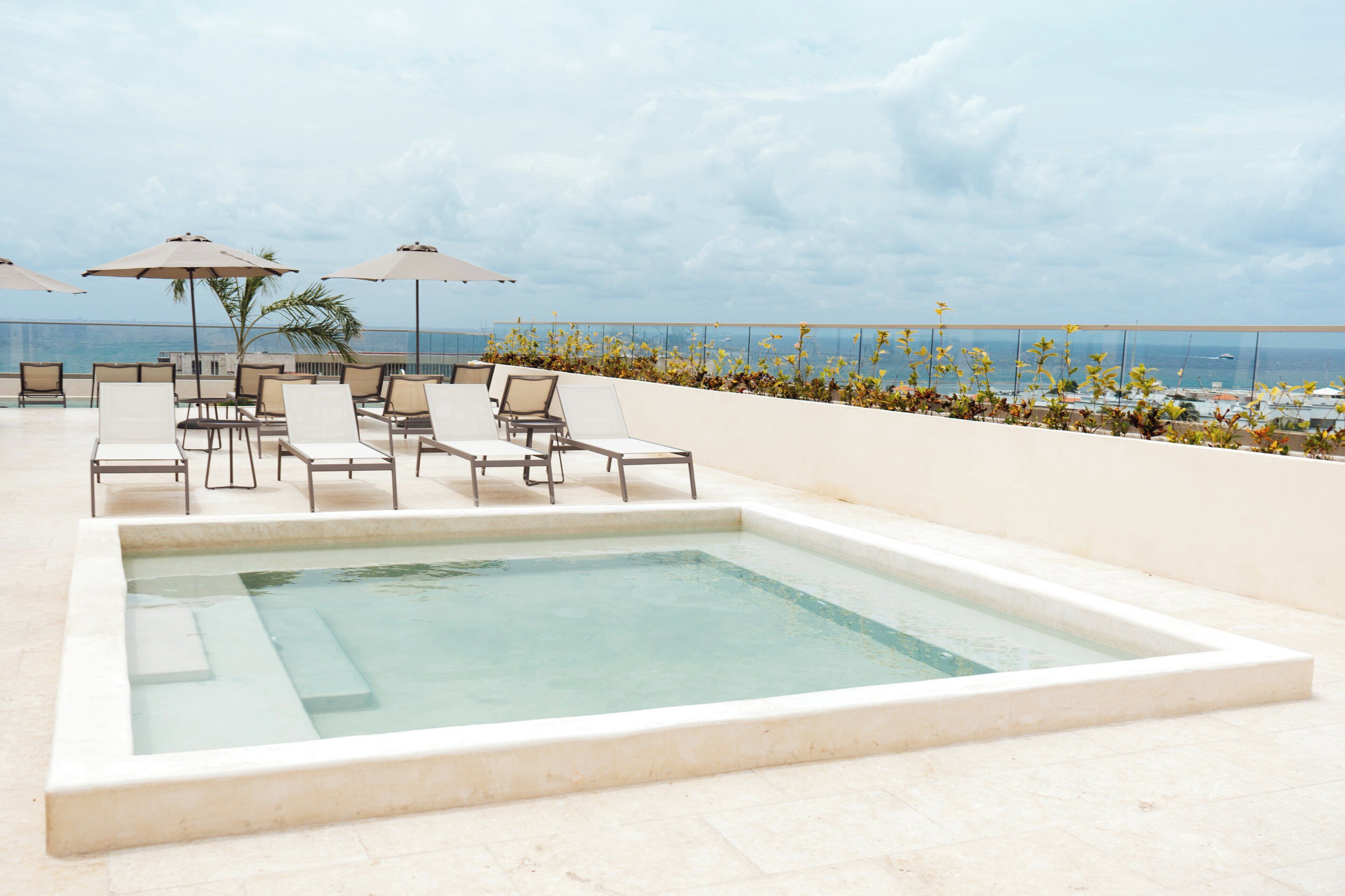 Ein Poolbereich auf dem Dach mit Liegestühlen und Sonnenschirmen mit Blick aufs Meer.