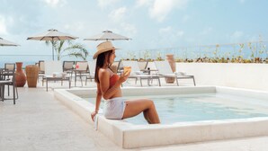 A woman sitting by a pool with lounge chairs and umbrellas in the background. - Hotel Indigo Playa Del Carmen by IHG (Playa del Carmen)