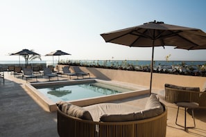 A rooftop pool area with lounge chairs, umbrellas, and a view of the sea.