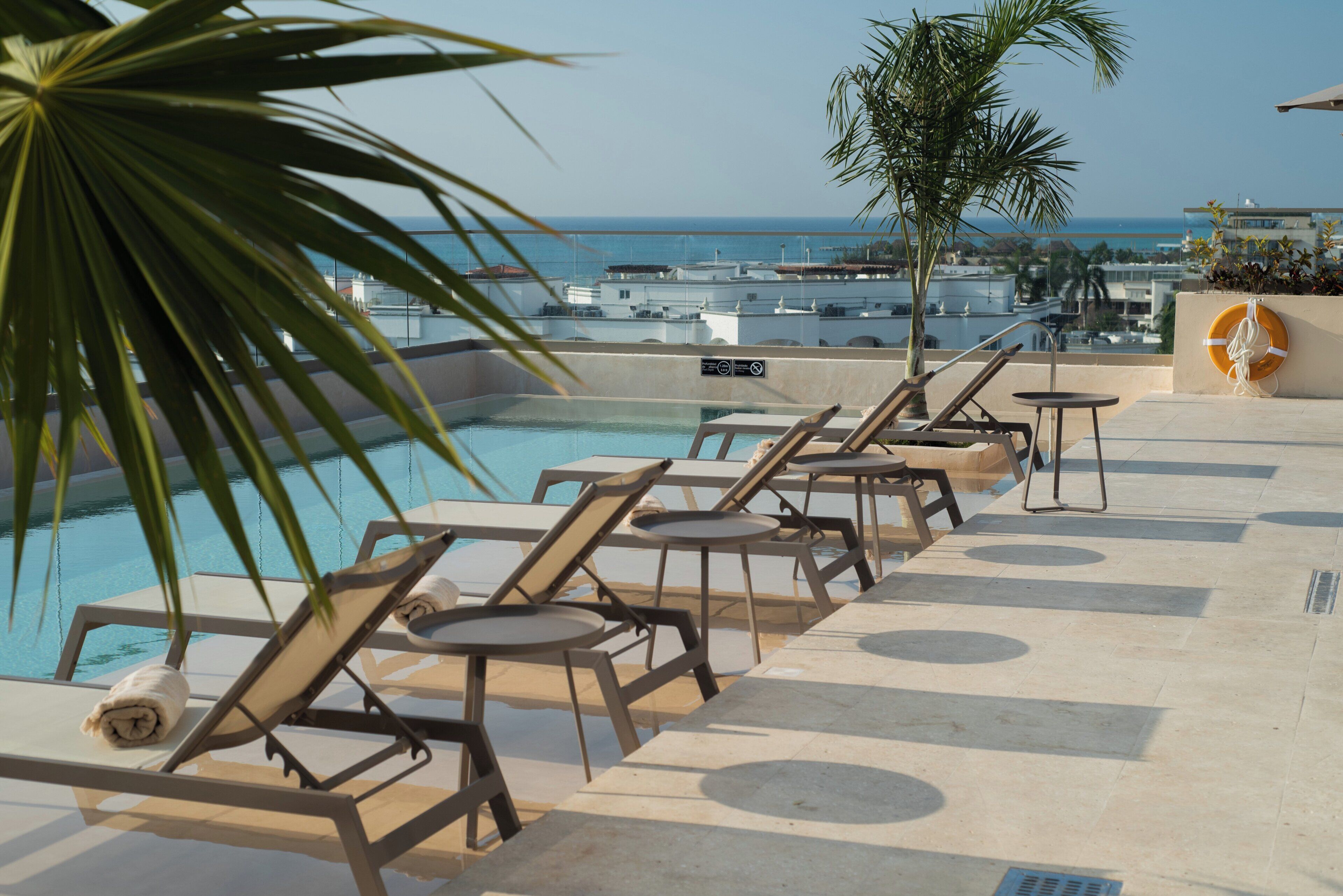 A poolside area with lounge chairs and a lifebuoy on a rooftop with a view of the sea.