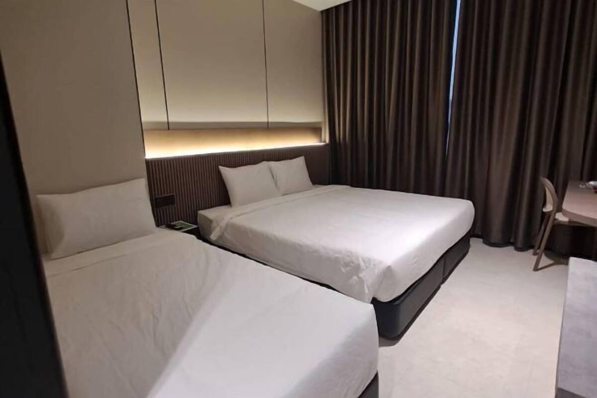 A hotel room with two beds, a desk, and a large window with curtains.