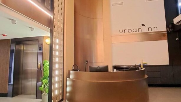 Modernilla tyylillä sisustettu vastaanottoalue, jossa on vastaanottotiski, kasvi ja seinä, jossa lukee teksti: ”urban inn”.