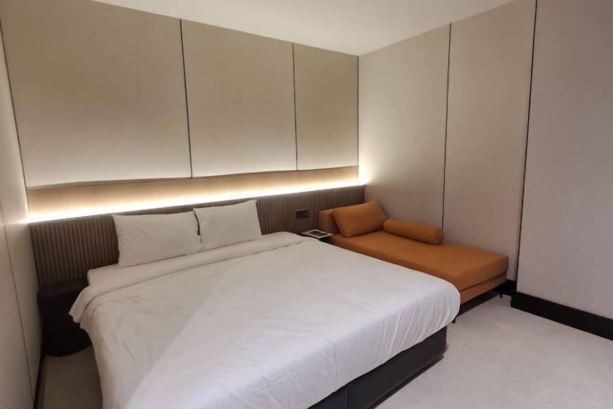 A modern bedroom with a large bed, a bedside table, a nightstand, and a sofa.