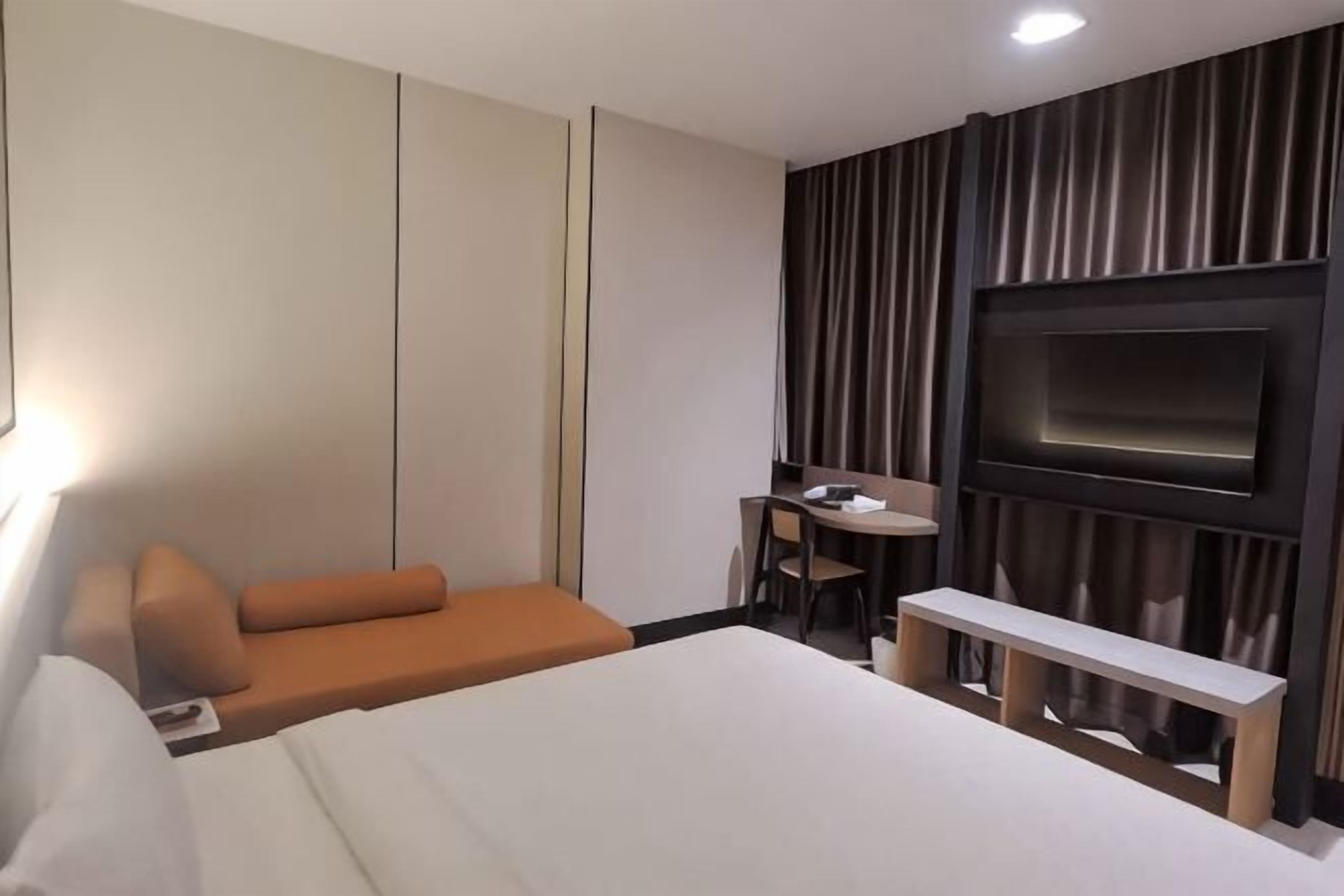 A hotel room with a bed, a desk, a chair, a TV, and a sofa.