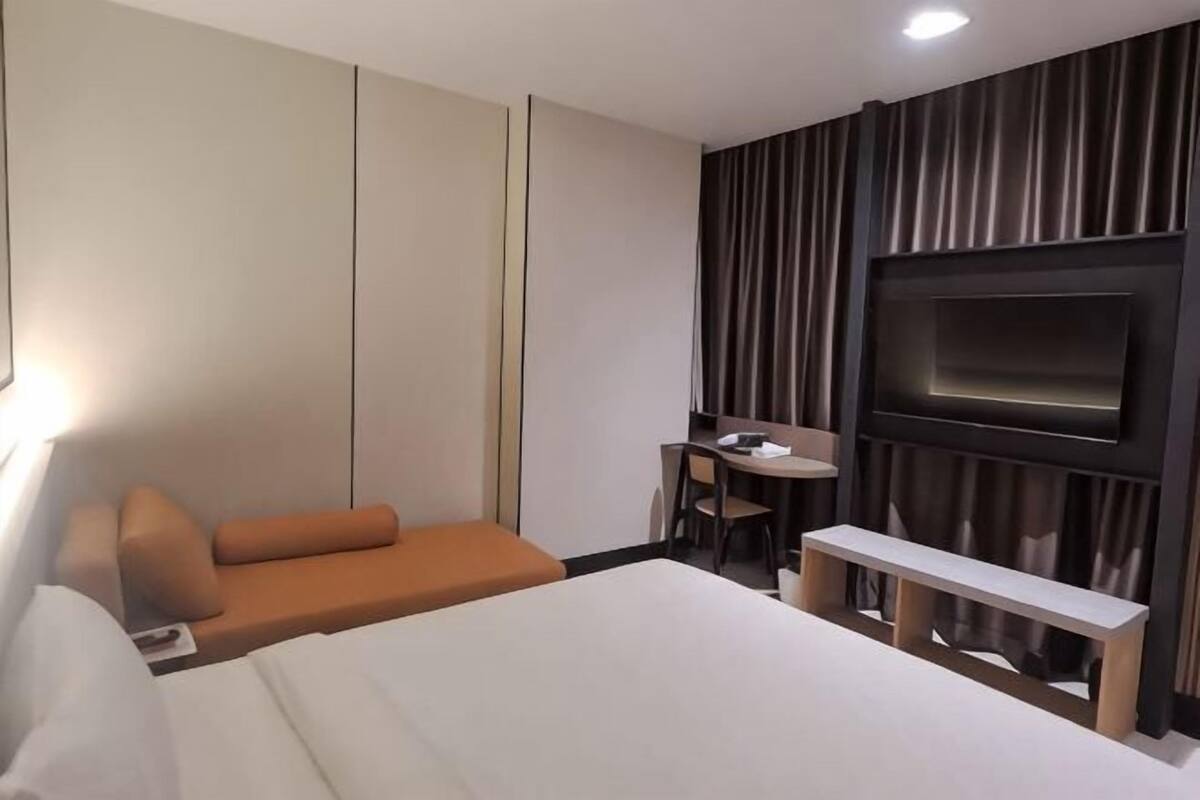 A hotel room with a bed, a desk, a chair, a TV, and a sofa.