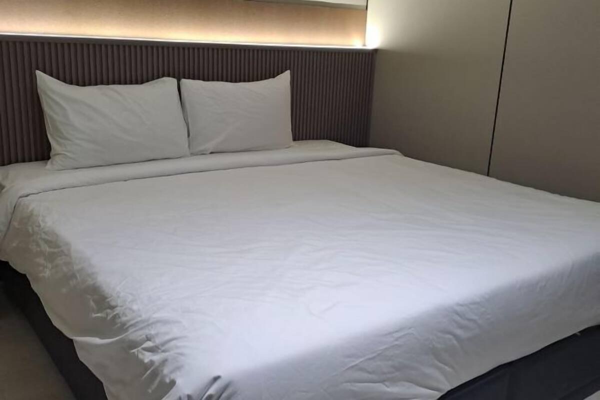 A neatly made bed with white linens and pillows, a headboard with vertical lines, and a wall panel.