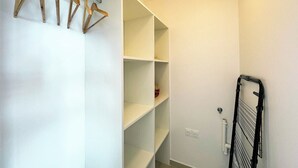 En rummelig garderobe med åbne hylder og et tørrestativ.