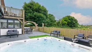 A hot tub in a backyard with a wooden deck, outdoor furniture, and a staircase leading to a balcony. - Bagend Sleeps 14 Hot Tub Balcony & Ping Pong (North Devon District)