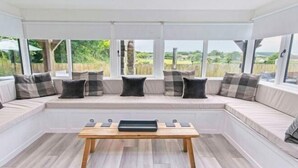 Habitación con zona de estar con banco incorporado, una mesa de madera y ventanas amplias con vistas al exterior.