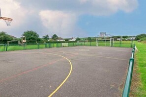Una cancha de baloncesto al aire libre con aro, rodeada por una valla verde.