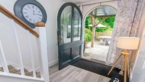 A staircase with a clock, a door leading to an outdoor patio, and a lamp. - Bagend Sleeps 14 Hot Tub Balcony & Ping Pong (North Devon District)