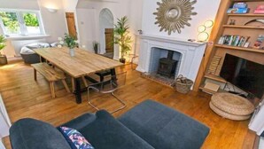 A spacious living room with a wooden dining table, a fireplace, and a bookshelf. - Bagend Sleeps 14 Hot Tub Balcony & Ping Pong (North Devon District)