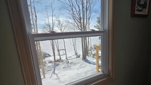 Ikkunasta avautuu näkymä lumiseen maisemaan ja paljaisiin puihin.