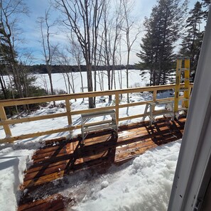 Un pontile in legno con ringhiera gialla affaccia su un paesaggio innevato e uno specchio d'acqua.