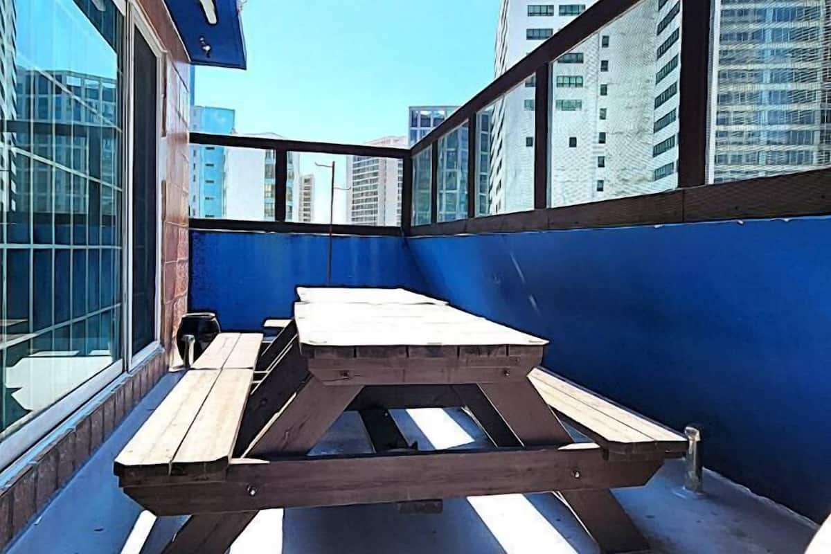 Une terrasse sur le toit, avec une table en bois et des bancs, entourée d’immeubles de grande hauteur.
