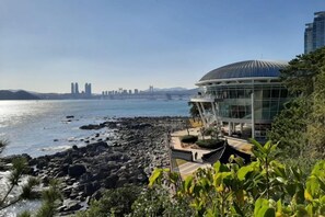 A coastal view with a modern building, a bridge, and a city skyline in the distance. - Sea Scenery Pension Haeundae (Busan)
