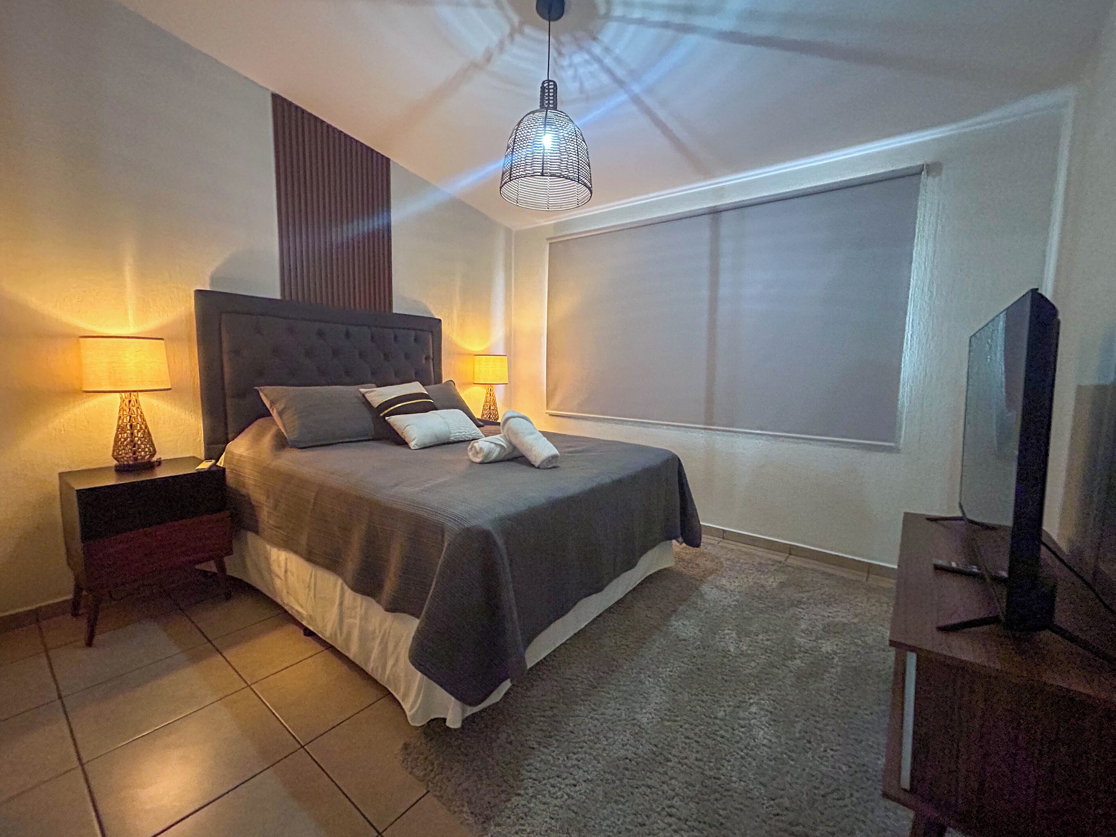 A neatly arranged bedroom with a bed, two bedside lamps, a television, and a large window.