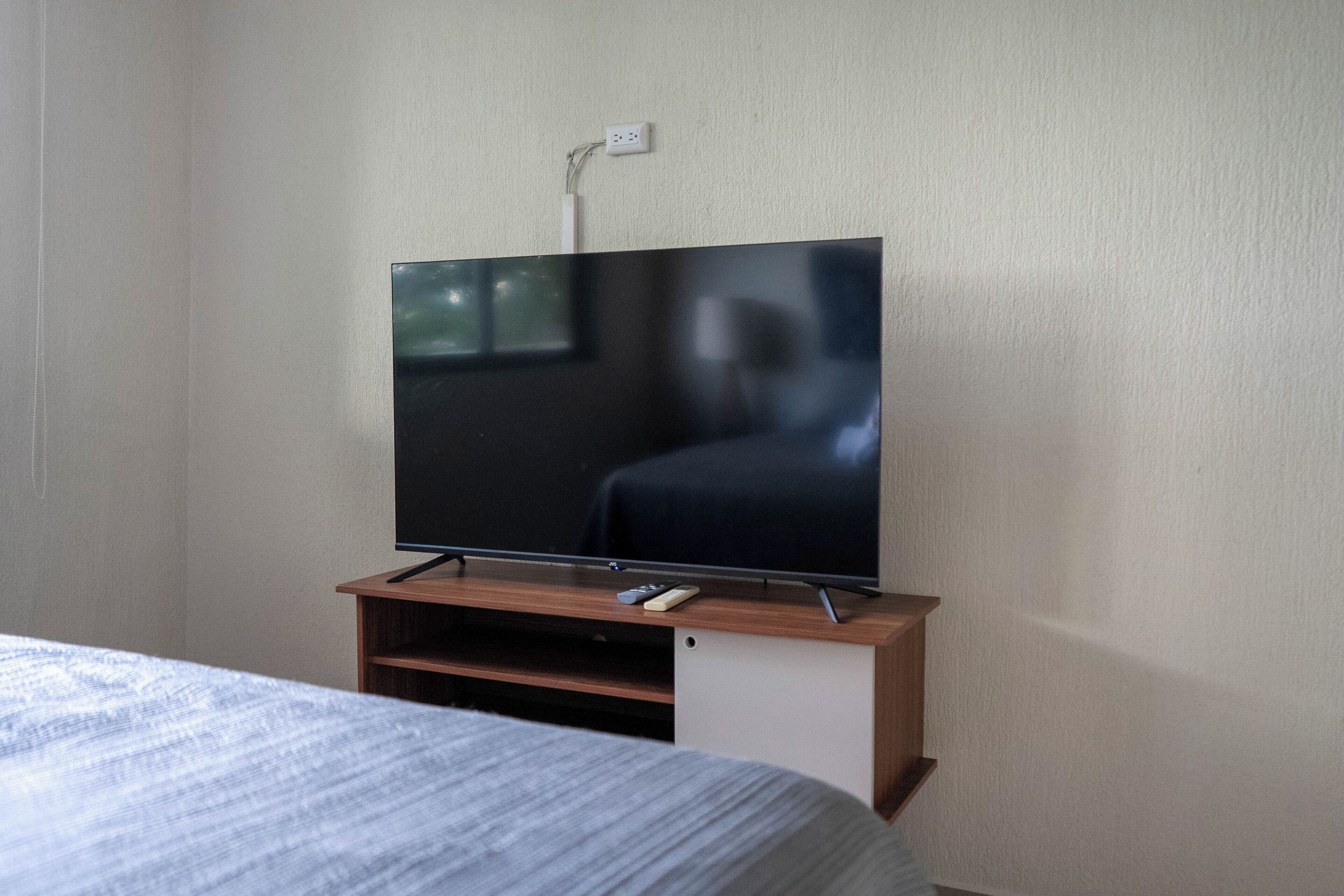 A television on a wooden stand in a room with a bed and a white wall.