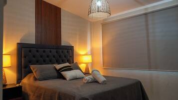 A neatly made bed with a dark headboard and pillows, a bedside lamp, and a hanging light fixture.