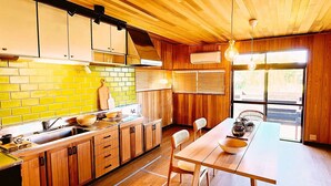 Une cuisine avec des meubles en bois, un mur de briques derrière l’évier, une table à manger avec des chaises et une grande fenêtre.
