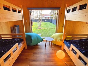 Une chambre avec des lits superposés, une petite table ronde et une vue sur une cour verdoyante.