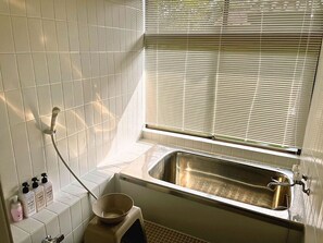 Une salle de bain équipée d’un lavabo, d’une douche et d’une fenêtre avec des stores.