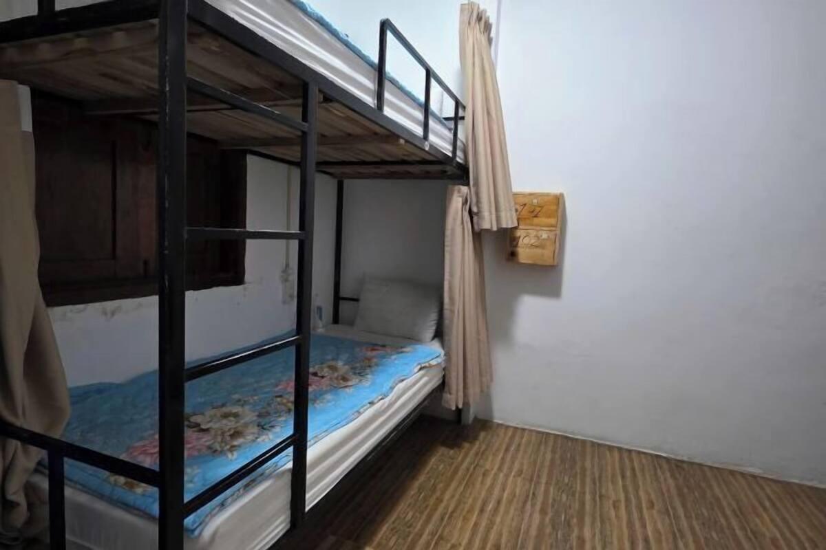 A bunk bed room with a wooden floor, a curtain, and a small wooden panel on the wall.