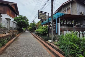 A narrow street with a sign for 'Aurora Hotel' and a building with a blue awning. - Aurora Backpackers Hostel (Luang Prabang)