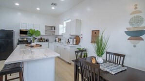 A modern kitchen with white cabinetry, a marble island, and a dining area with a dark wood table and chairs.