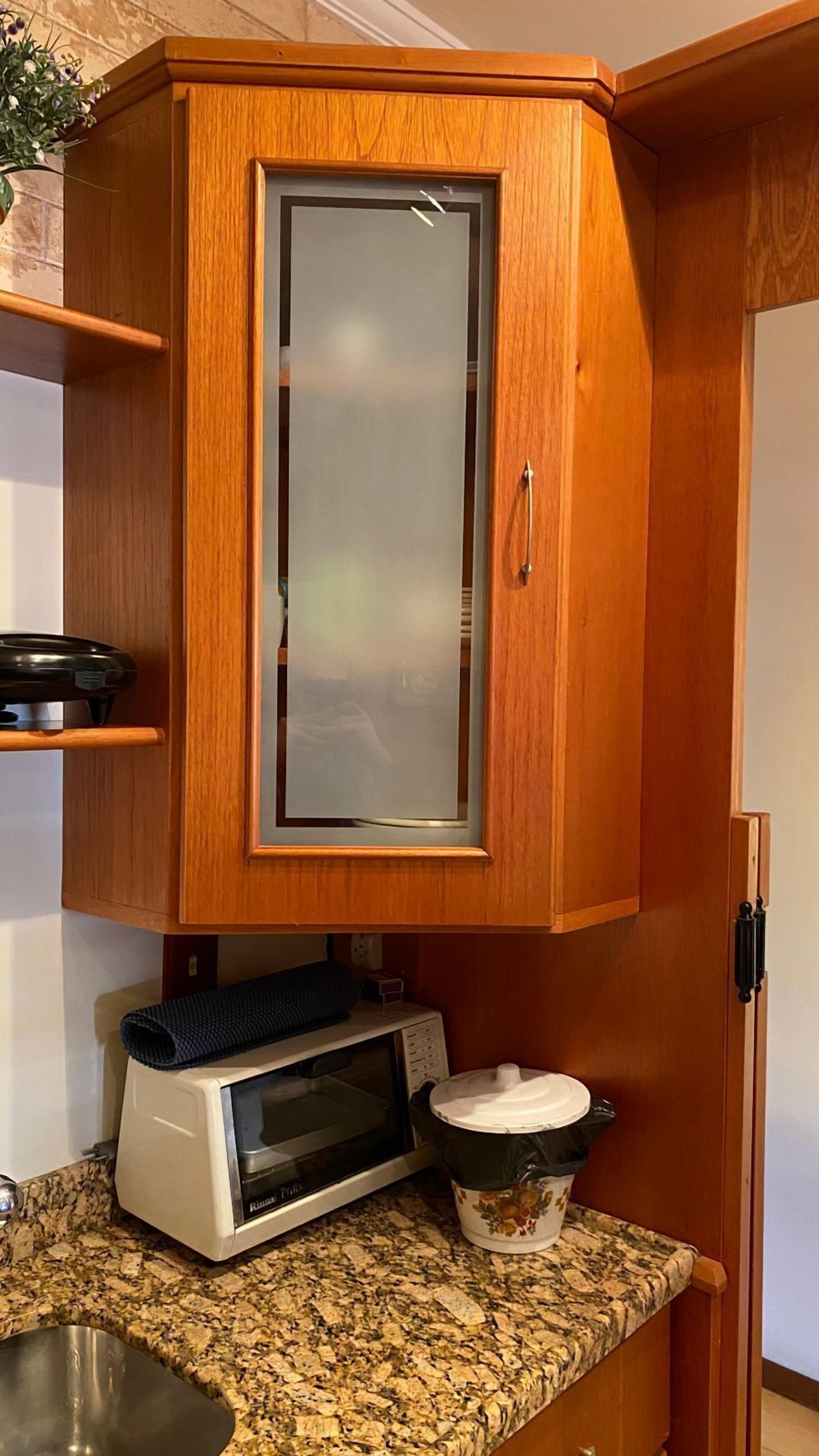 Una cocina con microondas, horno pequeño y un mueble de madera con puerta de vidrio.