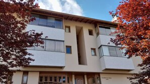 A multi-story building with a central entrance, a staircase leading to the entrance, and a small garden area with trimmed bushes. - Apartamento dos Pássaros - Mirante  (Gramado)
