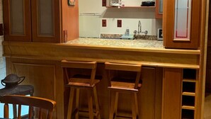 A kitchen with wooden cabinets, a coffee maker, and a sink. There are three wooden stools at the counter.