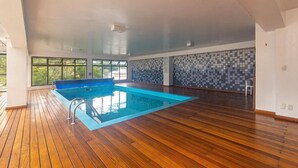 An indoor swimming pool with wooden flooring, large windows, and a tiled wall.