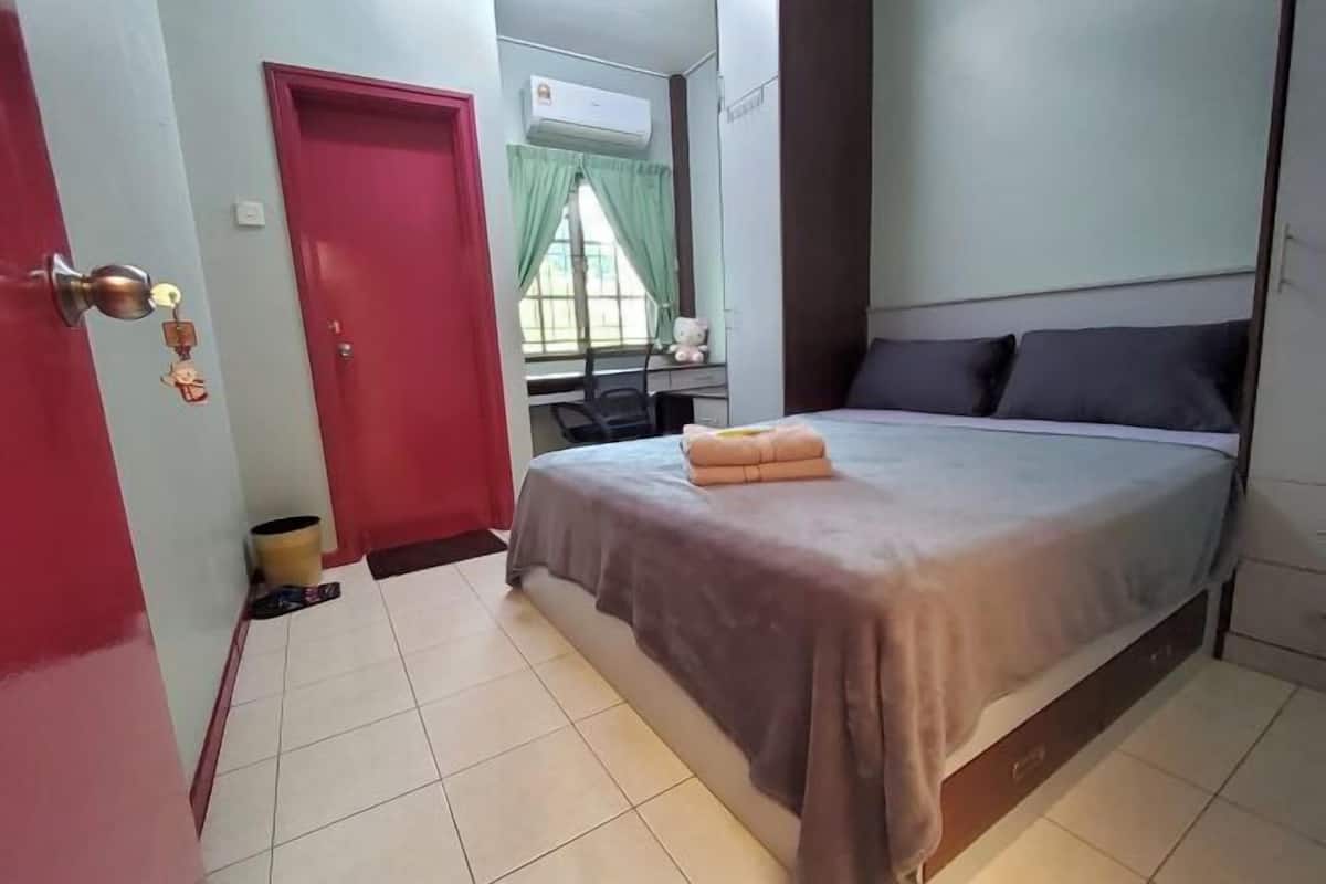A bedroom with a bed, a desk, a chair, a red door, and a window with curtains.