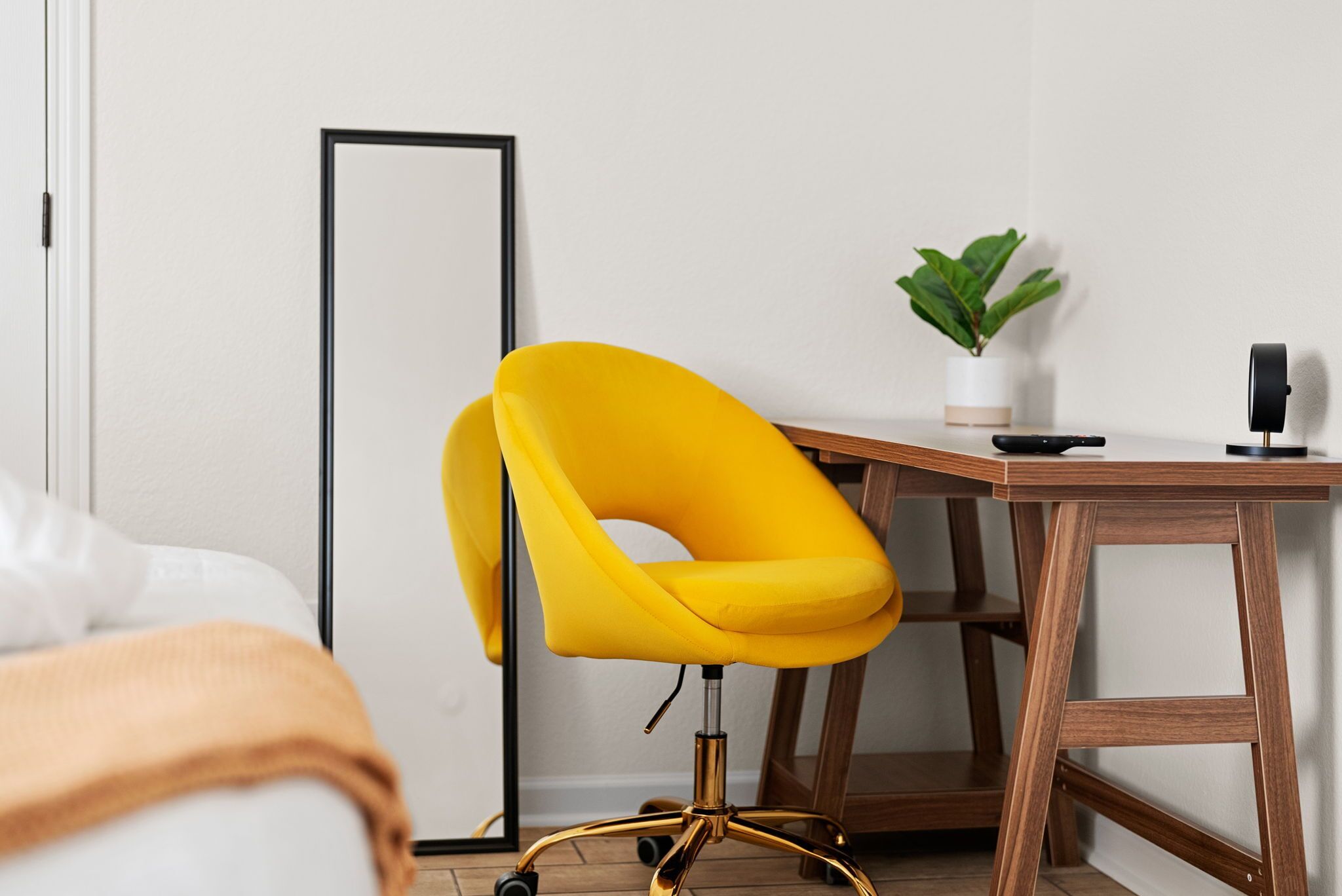 A room with a yellow chair, a wooden desk, a potted plant, and a floor lamp.