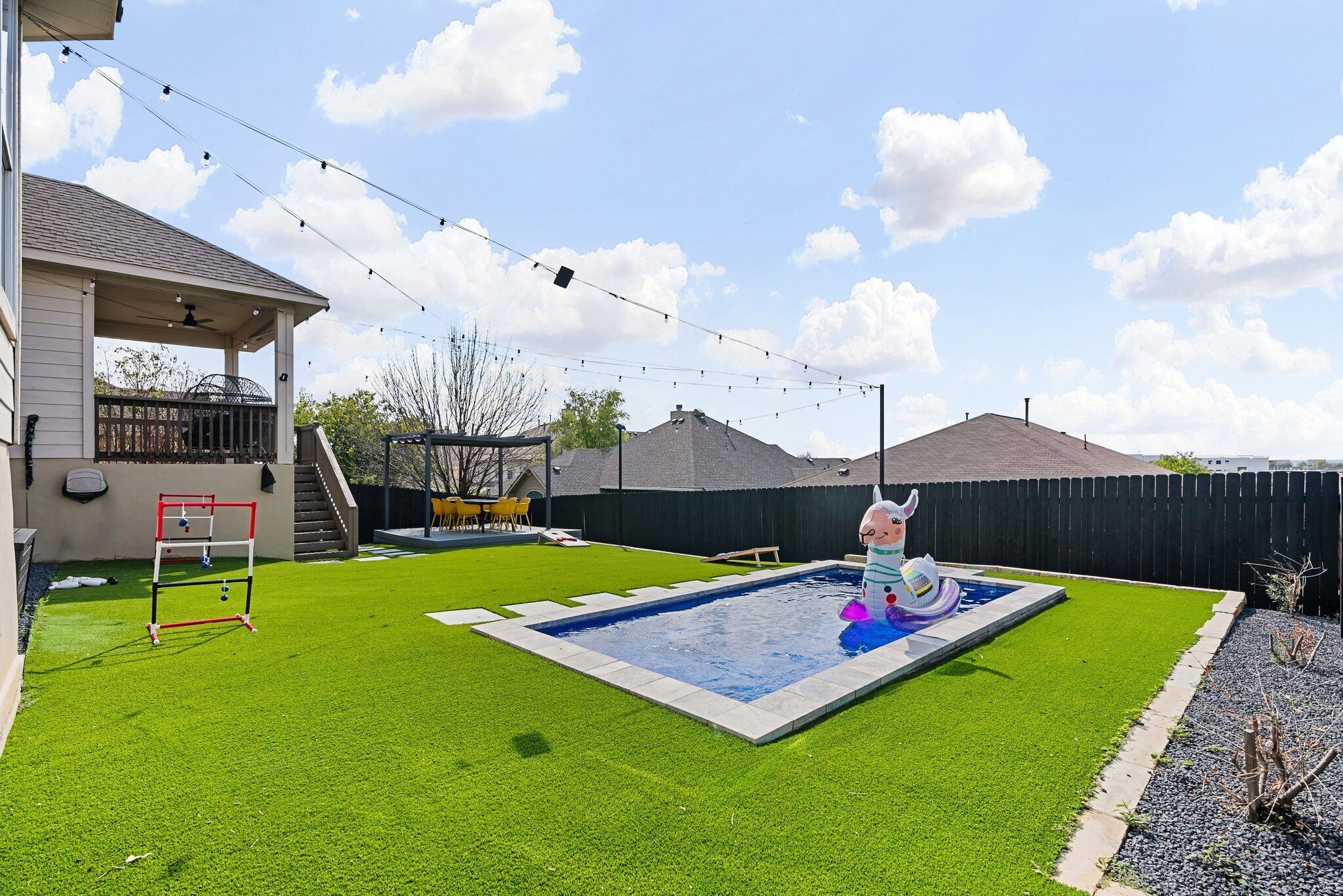A backyard with a swimming pool, artificial grass, a trampoline, and a fenced area.