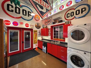 A retro-themed kitchen with red cabinets, a Whirlpool washer, and vintage gas station signs.
