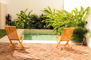 Two wooden chairs by a swimming pool with lush tropical plants around. - Casa Chicatana (Puerto Escondido)