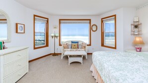 Ein Schlafzimmer mit Bett, Sitzbank, Kommode und Meerblick.